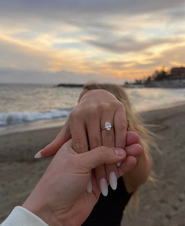 Zwei Hände mit Verlobungsring vor dem Sonnenuntergang am Meer