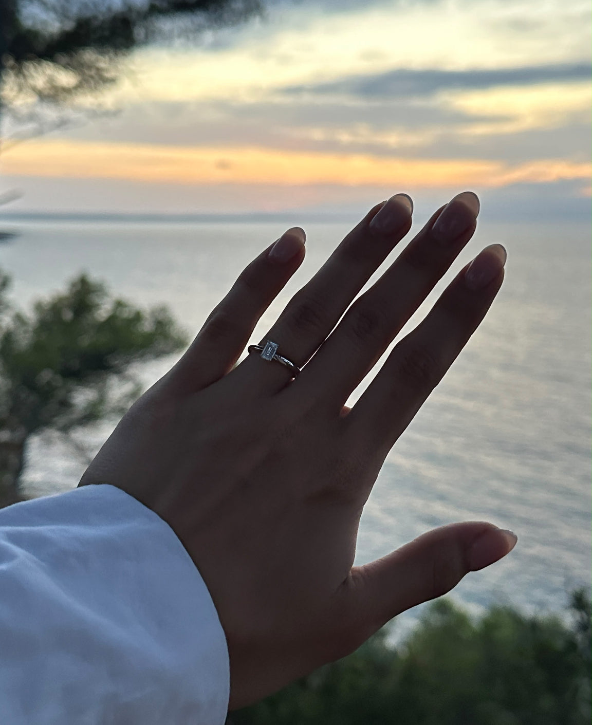 Hand mit Verlobungsring vor dem Sonnenuntergang am Meer