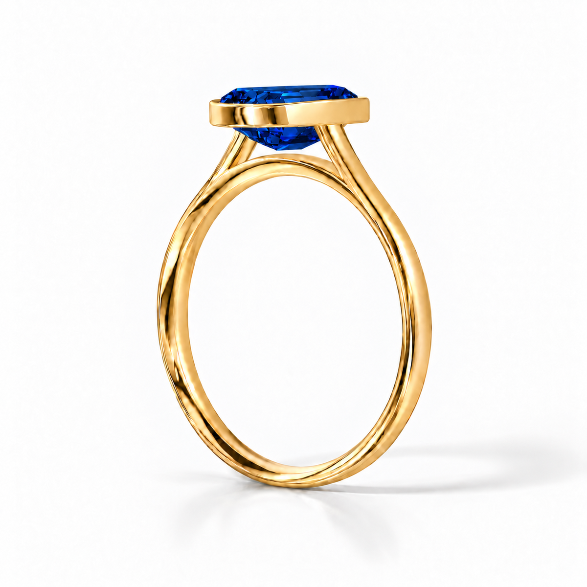 Gia Verlobungsring mit blauem Laborsaphir im Emerald-Schliff und Bezel-Fassung in Gelbgold – Schrägansicht auf weißem Hintergrund