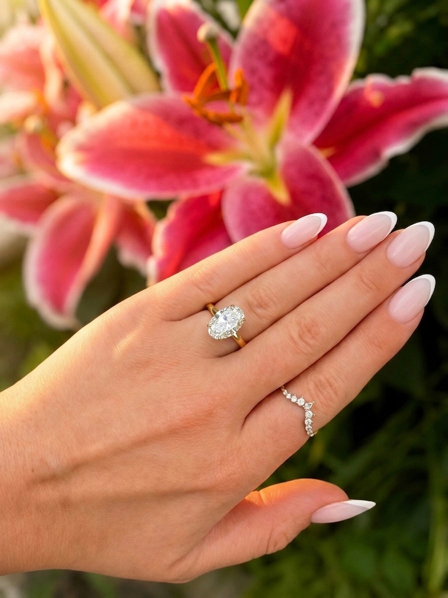 Ovaler Diamantring an einer Hand vor rosafarbenen Lilien