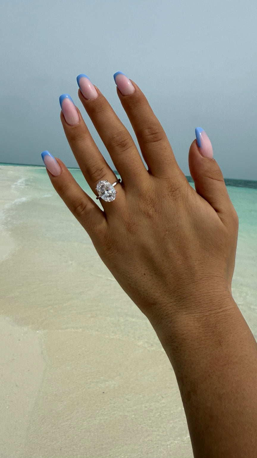 Ovaler Solitär-Diamantring an einer Hand vor dem Meer