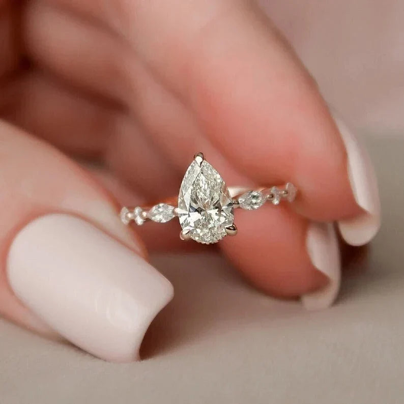 Tropfen-Verlobungsring mit seitlichen Diamanten zwischen zwei Fingern