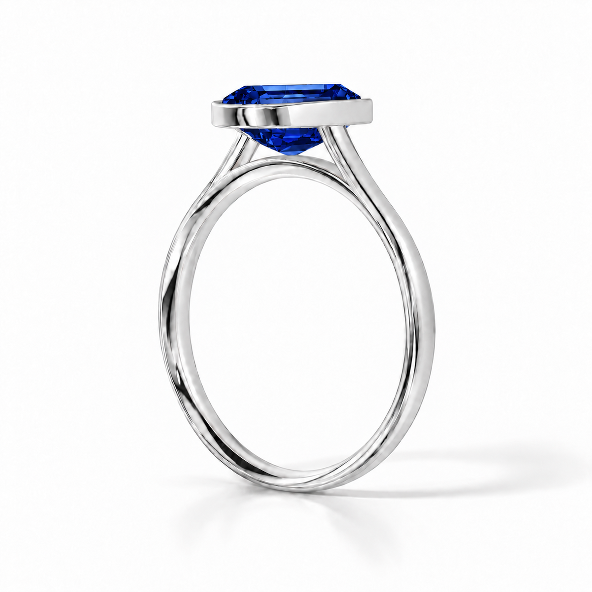 Gia Verlobungsring mit blauem Laborsaphir im Emerald-Schliff und Bezel-Fassung in Weißgold – Schrägansicht auf weißem Hintergrund