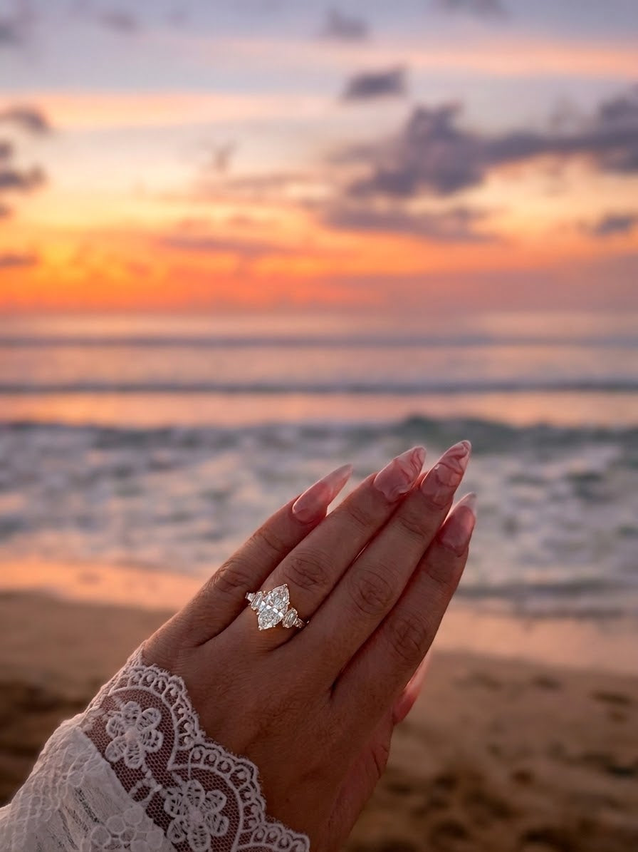 Marquise-Diamantring an einer Hand vor einem Sonnenuntergang am Meer